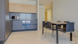 Une cuisine moderne avec des meubles gris, un four encastré et un coin repas comprenant une table et des chaises.