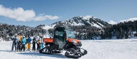 A snowmobile with a group of people standing beside it on a snowy field with mountains in the background.