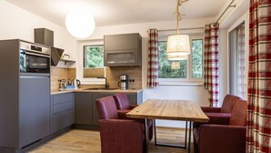 A compact kitchen with modern appliances, a dining area with a wooden table and red chairs, and large windows with plaid curtains. - Cosy apartment for 4 people with WIFI, TV and balcony (Brandstätter)