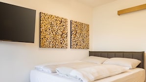 A neatly made bed with white linens and pillows, a grey upholstered headboard, and two wall-mounted artworks depicting logs. - Cosy apartment for 4 people with WIFI, TV and balcony (Brandstätter)