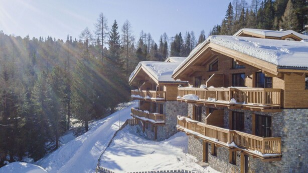 Eine mehrstöckige Holzlodge mit Balkonen, umgeben von schneebedeckten Bäumen und blauem Himmel.