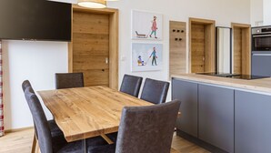 Eine moderne Küche mit Holztisch und -stühlen, einem eingebauten Ofen und Pendelleuchten.