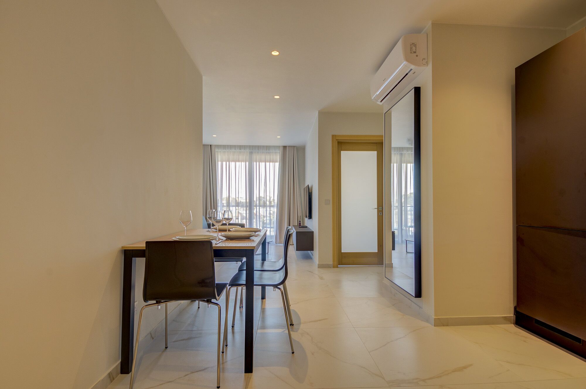 Une chambre d’hôtel moderne dotée d’un coin repas avec une table dressée pour quatre personnes, d’un canapé et d’un téléviseur fixé au mur.