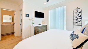 Un dormitorio con una cama, ventilador de techo, televisor, cómoda y una ventana con persianas.