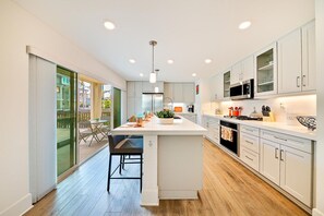 A modern kitchen with a central island, white cabinetry, and a dining area with a glass door leading outside.