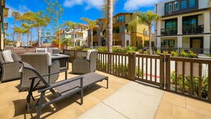 Un patio con mobiliario exterior, cercado por una valla de madera, y vistas a edificios de varios pisos con balcones.