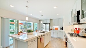Una cocina moderna con una isla grande, electrodomésticos de acero inoxidable y abundante luz natural gracias a amplias ventanas.