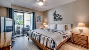 Een slaapkamer met een bed, een plafondventilator, een nachtkastje met een lamp, een bureau met een stoel, en een schuifdeur naar een buitengebied.