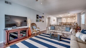 Een woonkamer met een televisie, bank, bijzettafeltje en een gestreept vloerkleed.