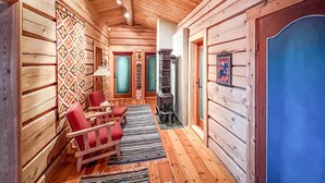 Interno di una baita con un camino, due poltrone rosse, una parete decorata e una porta blu.