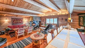 Accogliente interno di una baita in legno con camino, arredi in legno e una parete in pietra.
