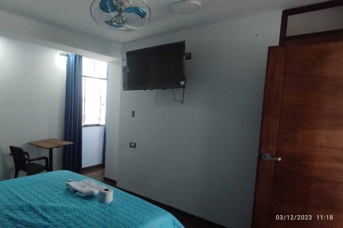 Ein Schlafzimmer mit Bett, Schreibtisch, Stuhl, Fernseher und einer Tür.