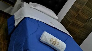 A bed with a blue mattress, white pillow, and a white towel with a logo. - Hotel Grand Paradise Marcona (Marcona)