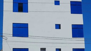 A multi-story building with a white facade and blue windows. The ground floor has a yellow entrance with a sign for "Hotel Grand Paradis." - Hotel Grand Paradise Marcona (Marcona)