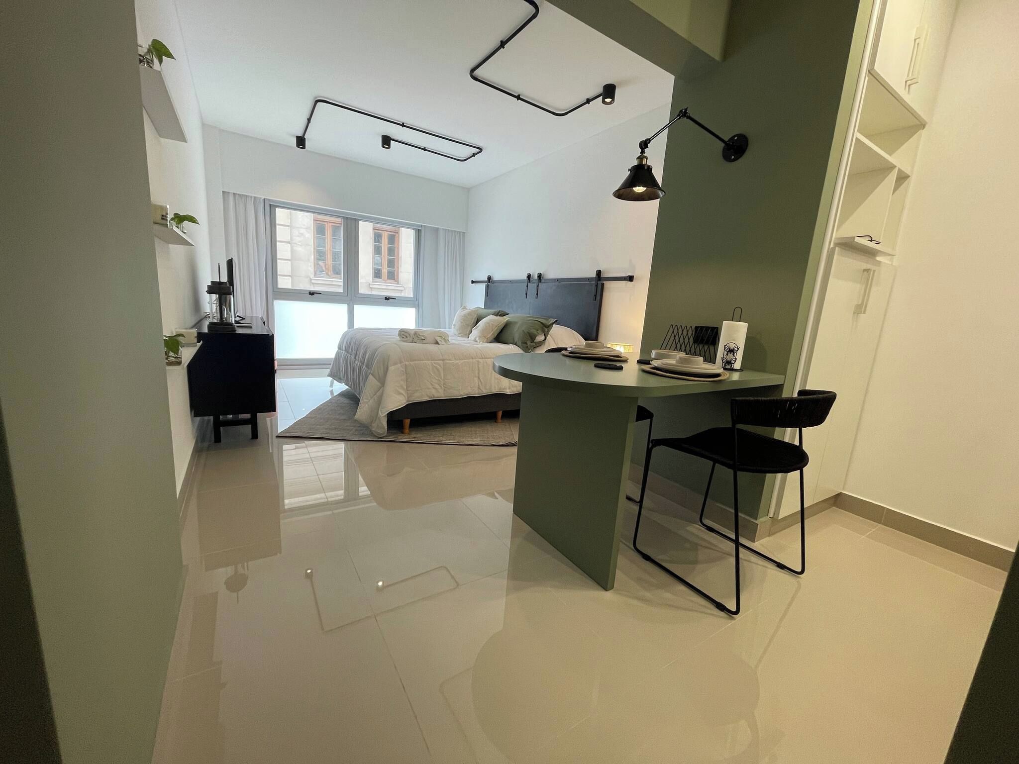 Quarto moderno com cama, mesa de cabeceira e um pequeno espaço de trabalho com cadeira.