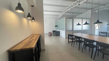Un espacio de oficina moderno con una larga mesa de madera y sillas negras, iluminación suspendida y un techo alto con vigas a la vista.