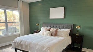 Un dormitorio con una cama grande, dos mesitas de noche, una pared verde y una ventana con cortinas.