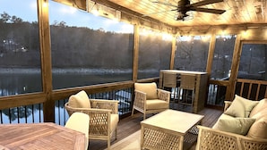 Una terraza cubierta al aire libre con muebles de mimbre, una mesa de madera y vista a un lago.