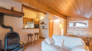 A cozy cabin interior with a fireplace, wooden walls, a white sofa, and a kitchen area. - Appartement Denali - Welkeys (Demi-Quartier)