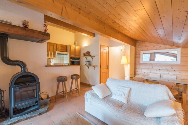 A cozy cabin interior with a fireplace, wooden walls, a white sofa, and a kitchen area.