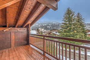 A wooden balcony with a view of a snowy mountain landscape and a pine tree.