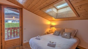 A bedroom with a wooden ceiling, a skylight, a bed with white bedding, and a view of a building through a glass door. - Appartement Denali - Welkeys (Demi-Quartier)