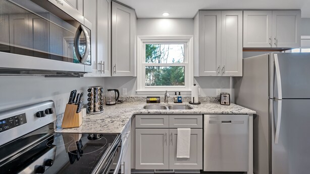 Una cocina moderna con armarios blancos, un refrigerador de acero inoxidable, un lavamanos doble y una ventana sobre el lavamanos.