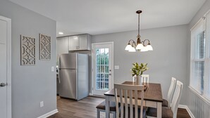 Una cocina moderna con un refrigerador de acero inoxidable, una mesa de comedor con sillas y una lámpara colgante.