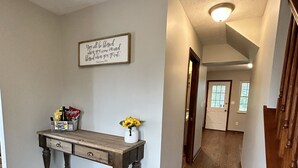 Ein Flur mit Holzboden, einer Holzbank mit Schubladen, einer Vase mit Sonnenblumen und einem gerahmten Motivationsspruch an der Wand.