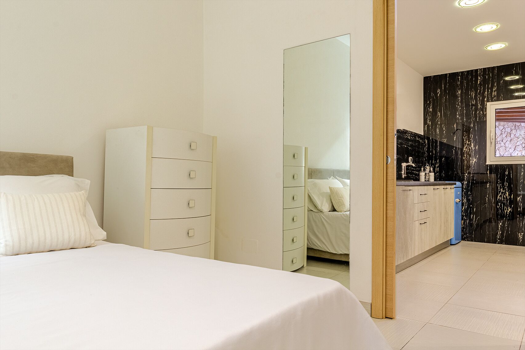 Una habitación de hotel con cama, cómoda, espejo y kitchenette.