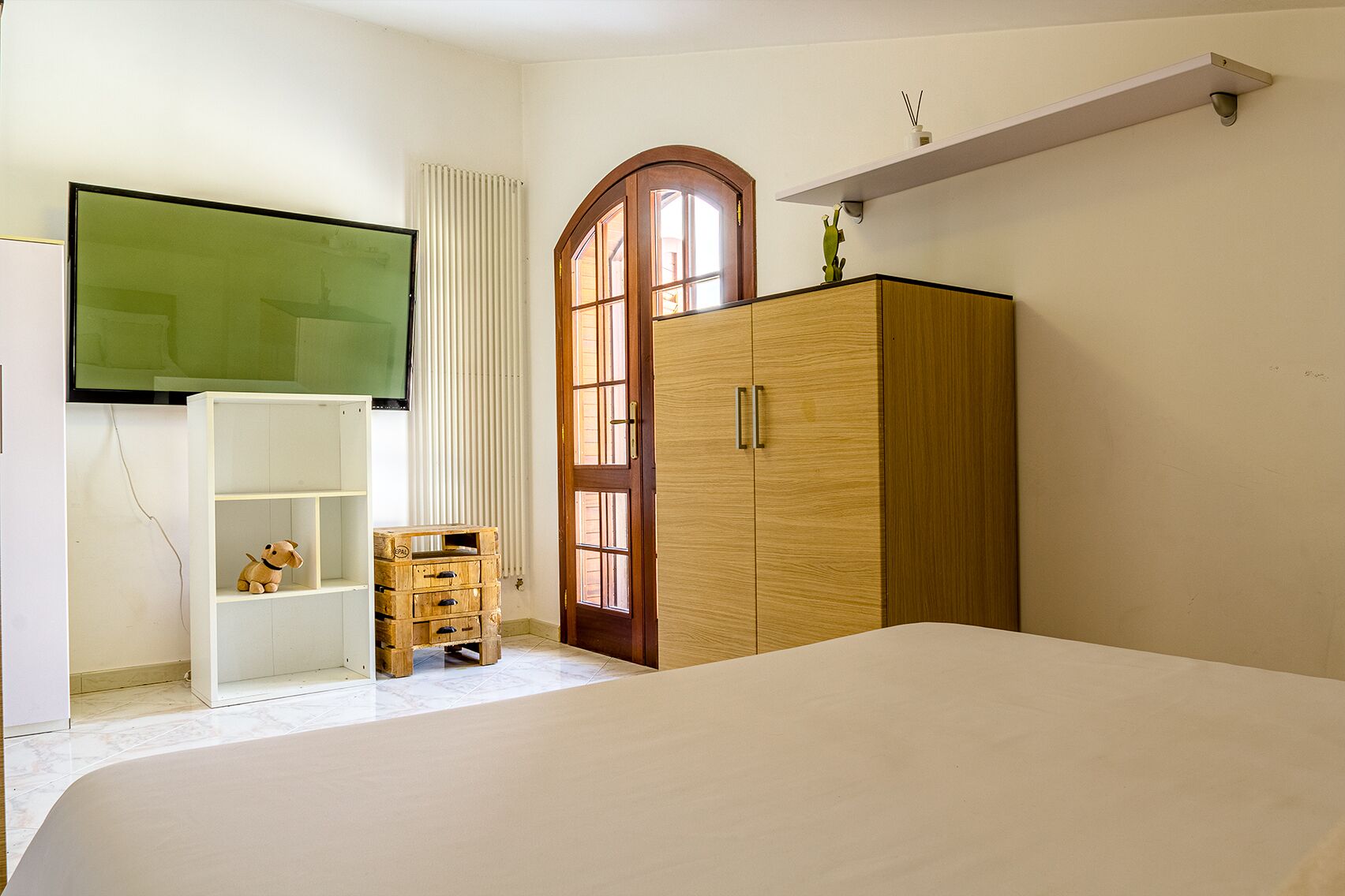 Une chambre à coucher comprenant un lit, une armoire en bois, une petite commode en bois, une étagère blanche et une fenêtre avec un cadre vert.