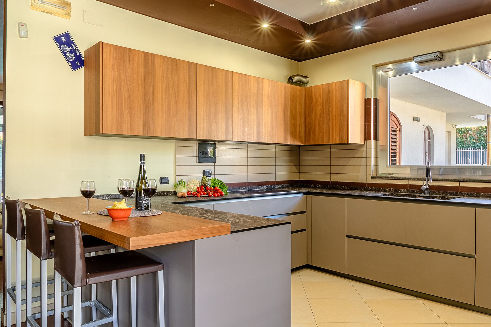 A modern kitchen with wooden cabinets, a marble countertop, and a built-in island. There is a dining area with a table and chairs, and a window providing natural light.