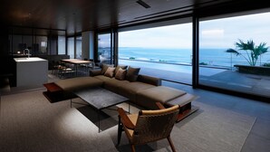 A modern living room with a large sectional sofa, a dining area, and a view of the ocean. - NOT A HOTEL AOSHIMA (Miyazaki)