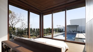 A modern bedroom with a large window overlooking a swimming pool and garden. - NOT A HOTEL AOSHIMA (Miyazaki)