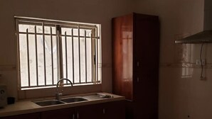 A kitchen with a window, a sink, cabinets, and a trash bin. - SMART DWELLINGS (Brufut)