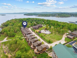 A lakeside resort with wooden cabins, a central building with a pool, and a view of the lake. - Scenic Lakefront Lodge w/ Private Hot Tub, Boat Slip, Wraparound Deck & Free Attractions (Branson)