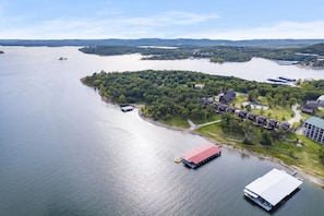 Vue aérienne d’une propriété au bord du lac, avec un quai, un bâtiment à toit rouge et un ensemble de maisons entourées de verdure.