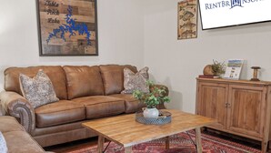 A living room with a brown leather sofa, a wooden coffee table, a patterned rug, and a cabinet with a sign on top. - Scenic Lakefront Lodge w/ Private Hot Tub, Boat Slip, Wraparound Deck & Free Attractions (Branson)