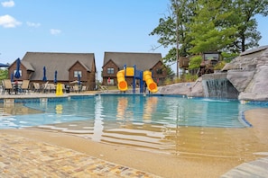 Une piscine avec un toboggan, des chaises longues et un bâtiment en bois en arrière-plan.