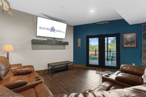 Un salon avec des canapés en cuir, un téléviseur fixé au mur, un banc et une vue sur l’extérieur, visible à travers une porte vitrée.