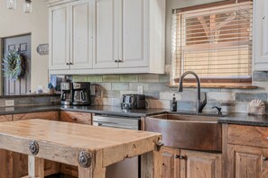 A kitchen with white cabinets, a wooden table, a sink, and a window with blinds.