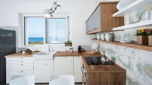 A modern kitchen with a view of the sea, wooden cabinets, white countertops, and a coffee machine.