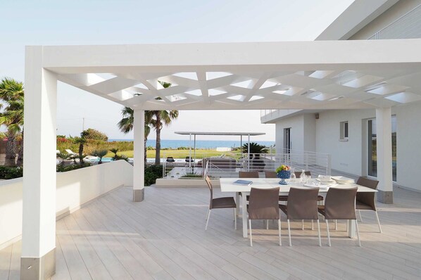 An outdoor patio with a white pergola, a dining table set for four, and a view of the ocean.