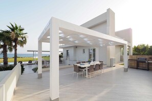 A modern outdoor patio with a dining area, a pergola, and a view of the sea. - Wonderful private villa with private pool, WIFI, sauna, hot tub, A/C, TV, patio and panoramic view (Marina Di Modica)