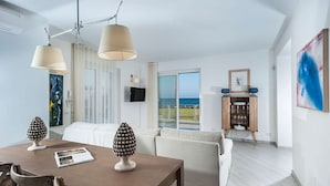 A modern living room with a dining area, large windows with a view, and a flat-screen TV mounted on the wall.