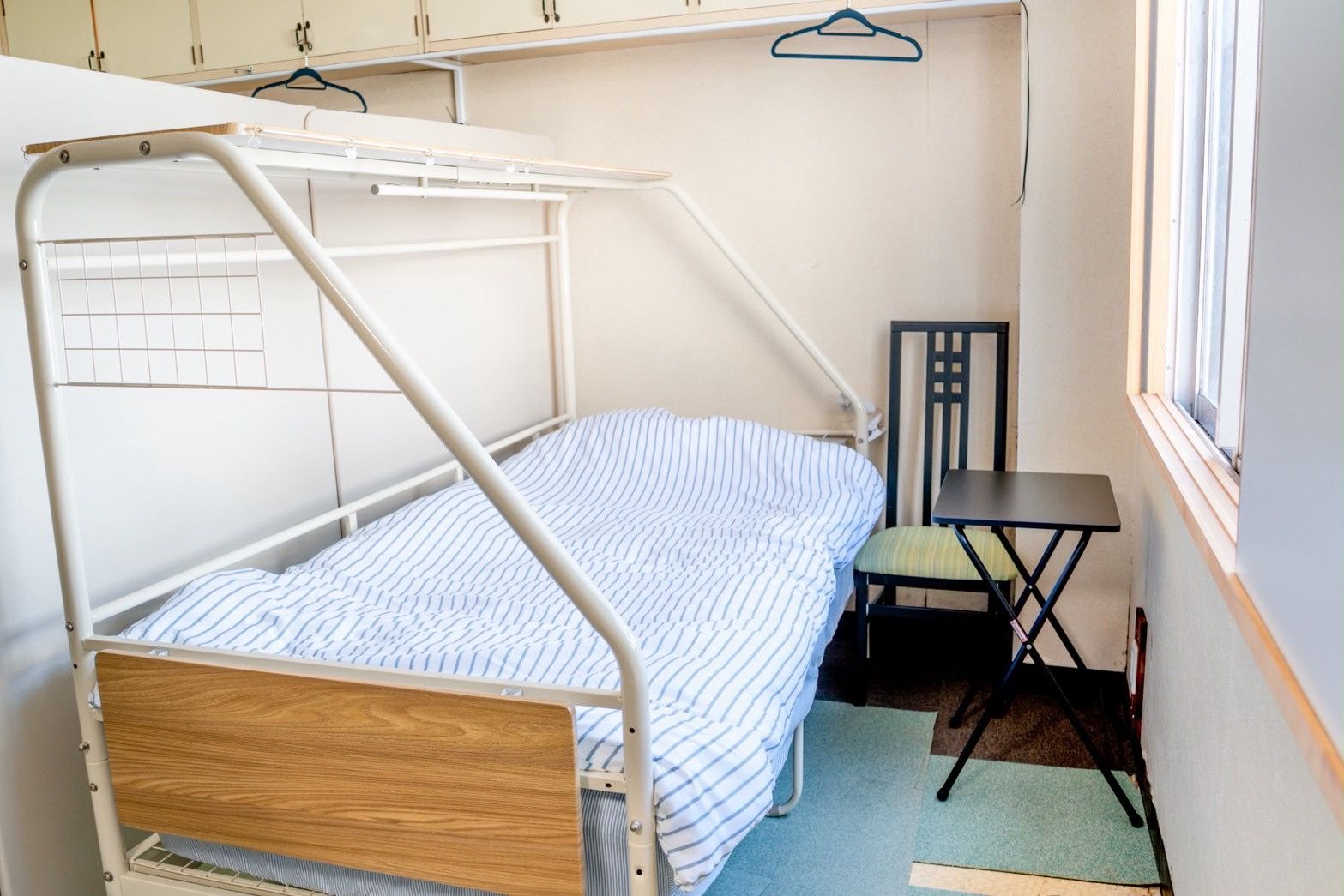 A single-bed room with a wooden headboard, a small table, and a chair.