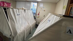 A hotel room with two beds covered in white sheets, each bed marked with a number. There is a window with a view of a blue building outside, and the room has a tiled floor. - guest house aroma - Hostel (Ureshino)