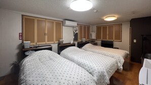 A hotel room with two beds, wooden wardrobes, a small desk with a lamp, and a ceiling light. - guest house aroma - Hostel (Ureshino)