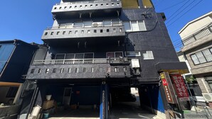 A multi-story building with a garage entrance, air conditioning units, and a sign indicating a business on the ground floor. - guest house aroma - Hostel (Ureshino)