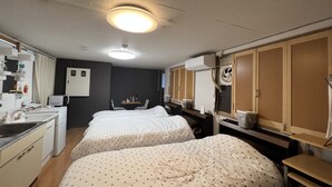 A compact hotel room with two beds, a kitchenette, a small table, and a ceiling fan. - guest house aroma - Hostel (Ureshino)